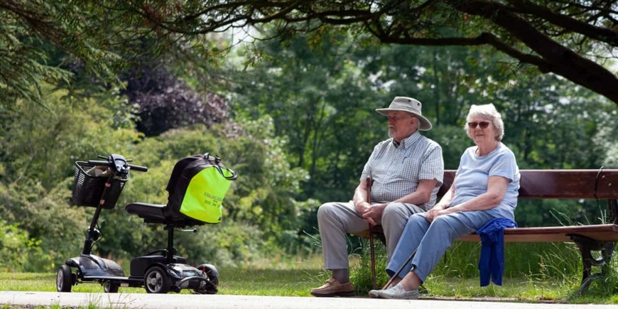 Senior couple on park bench with mobility scooter